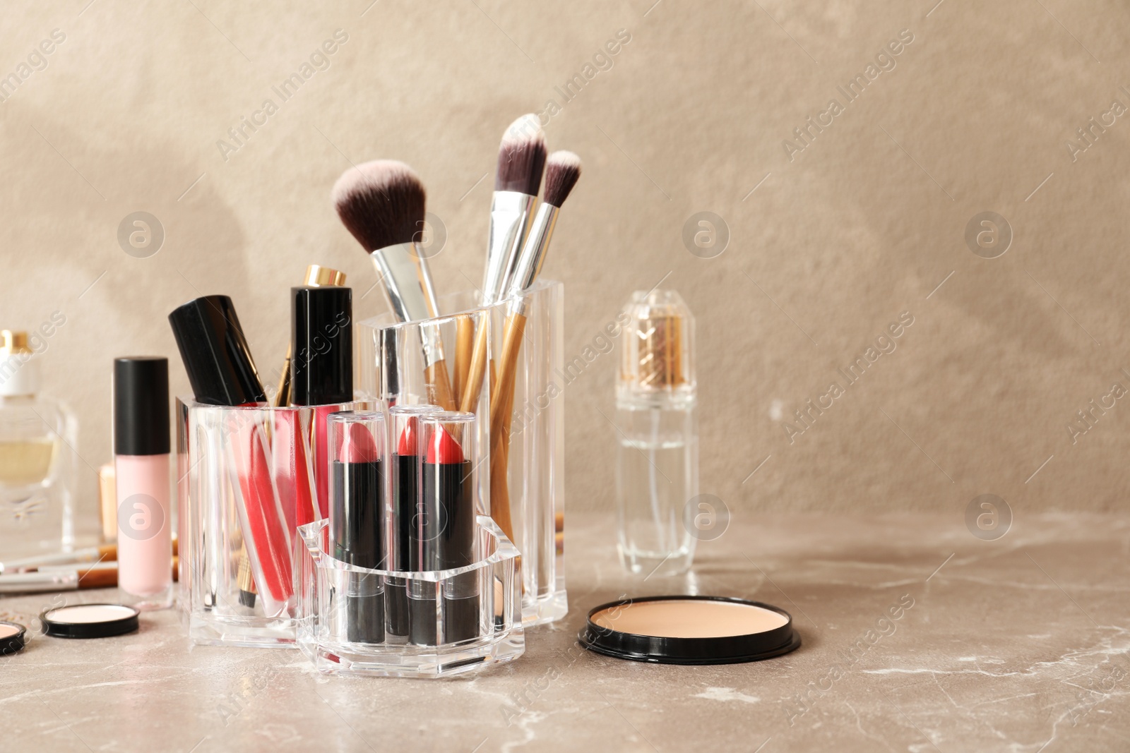 Photo of Lipstick holder with different makeup products on table against color background. Space for text