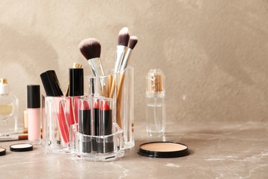 Photo of Lipstick holder with different makeup products on table against color background. Space for text