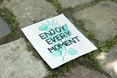 Photo of Card with phrase Enjoy Every Moment on ground