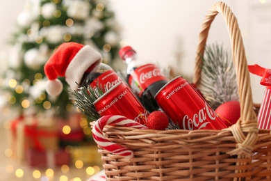 Photo of MYKOLAIV, UKRAINE - January 01, 2021: Basket with Coca-Cola drinks against blurred Christmas tree