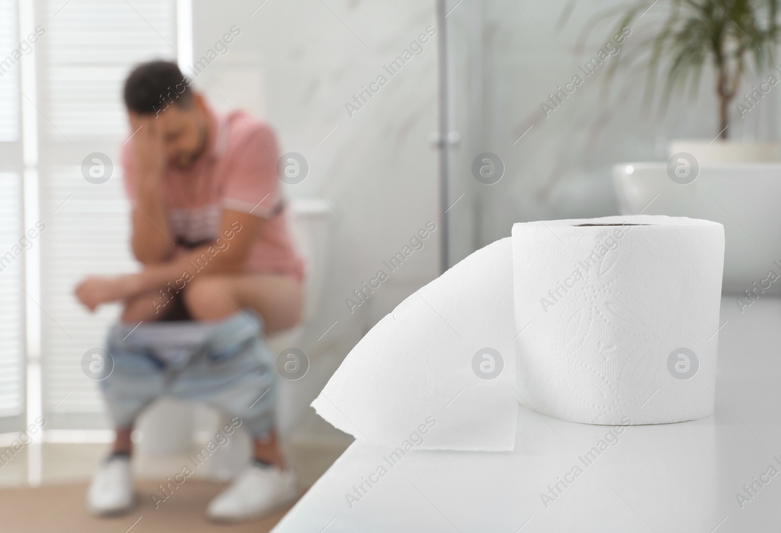 Photo of Man suffering from hemorrhoid in rest room, focus on toilet paper