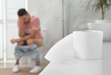 Man suffering from hemorrhoid in rest room, focus on toilet paper