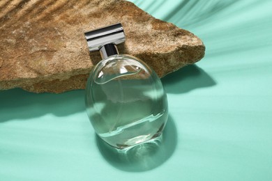 Bottle of luxury perfume in sunlight and stone on turquoise background, above view