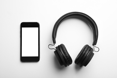 Stylish headphones and modern phone on white background, top view. Space for text