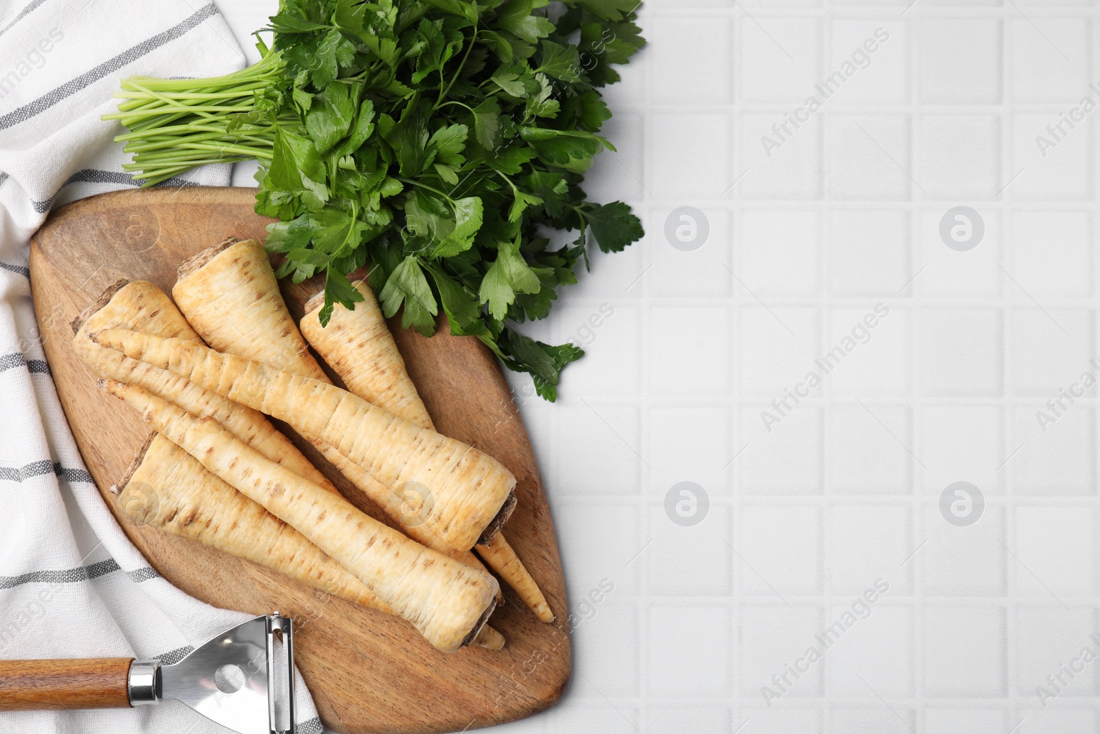 Photo of Raw parsley roots, bunch of fresh herb and peeler on white table, flat lay. Space for text