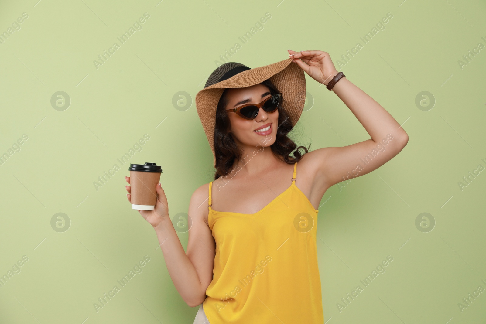 Photo of Beautiful young woman with straw hat and cup of coffee on light green background