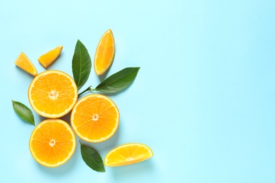 Fresh oranges and leaves on color background, flat lay with space for text. Citrus fruits