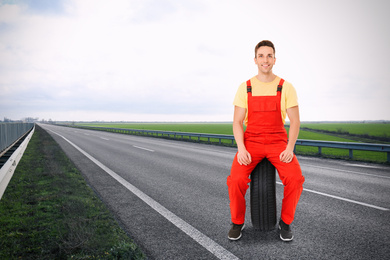 Image of Mechanic with car tire on asphalt highway outdoors, space for text