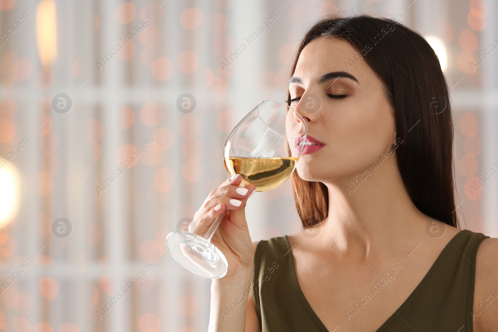 Photo of Beautiful young woman with glass of luxury white wine indoors. Space for text