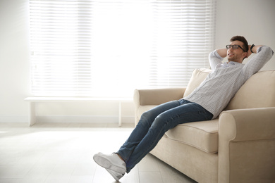 Photo of Young man relaxing on couch near window at home. Space for text