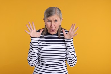 Portrait of surprised senior woman on yellow background