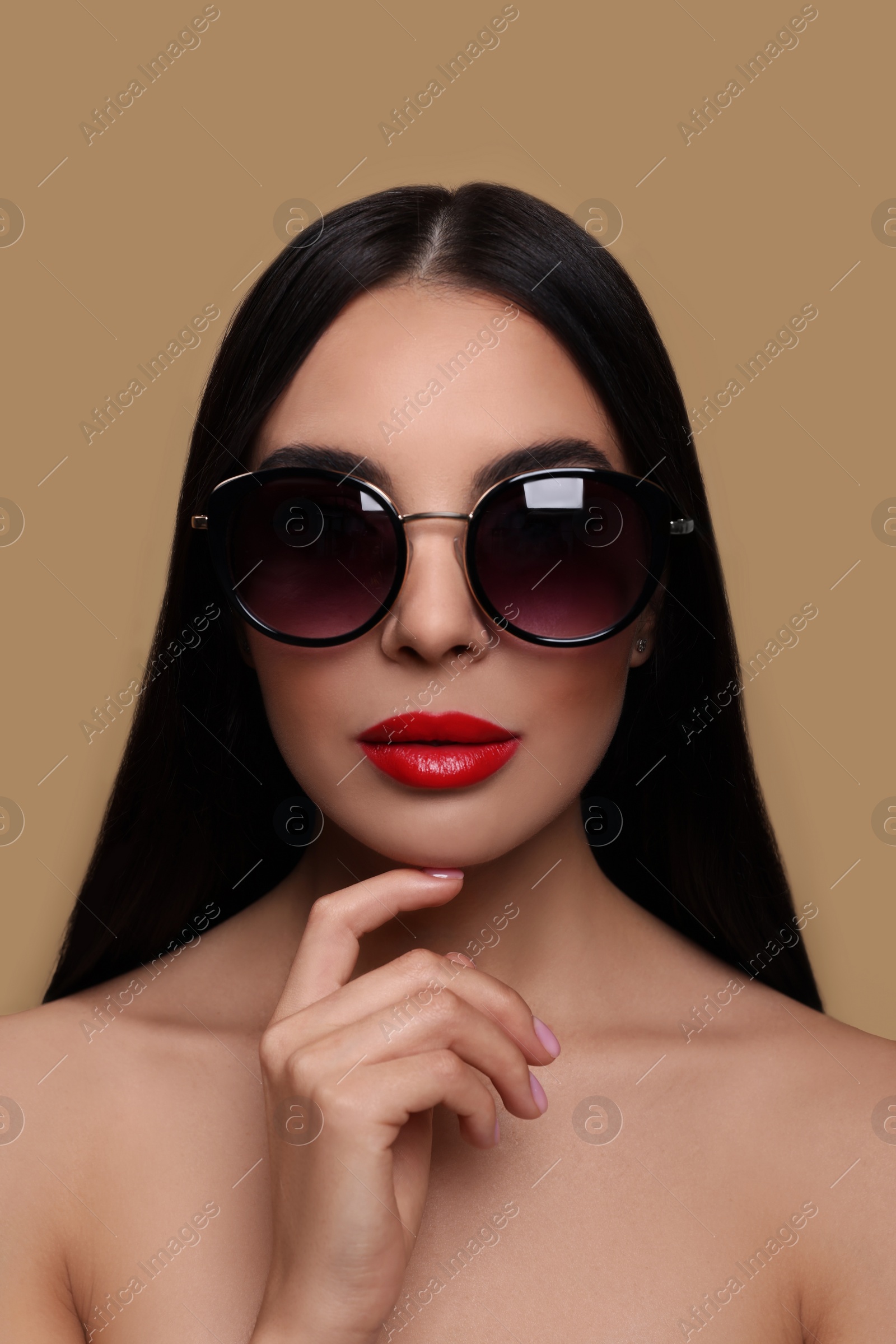 Photo of Attractive woman in fashionable sunglasses touching her face against beige background