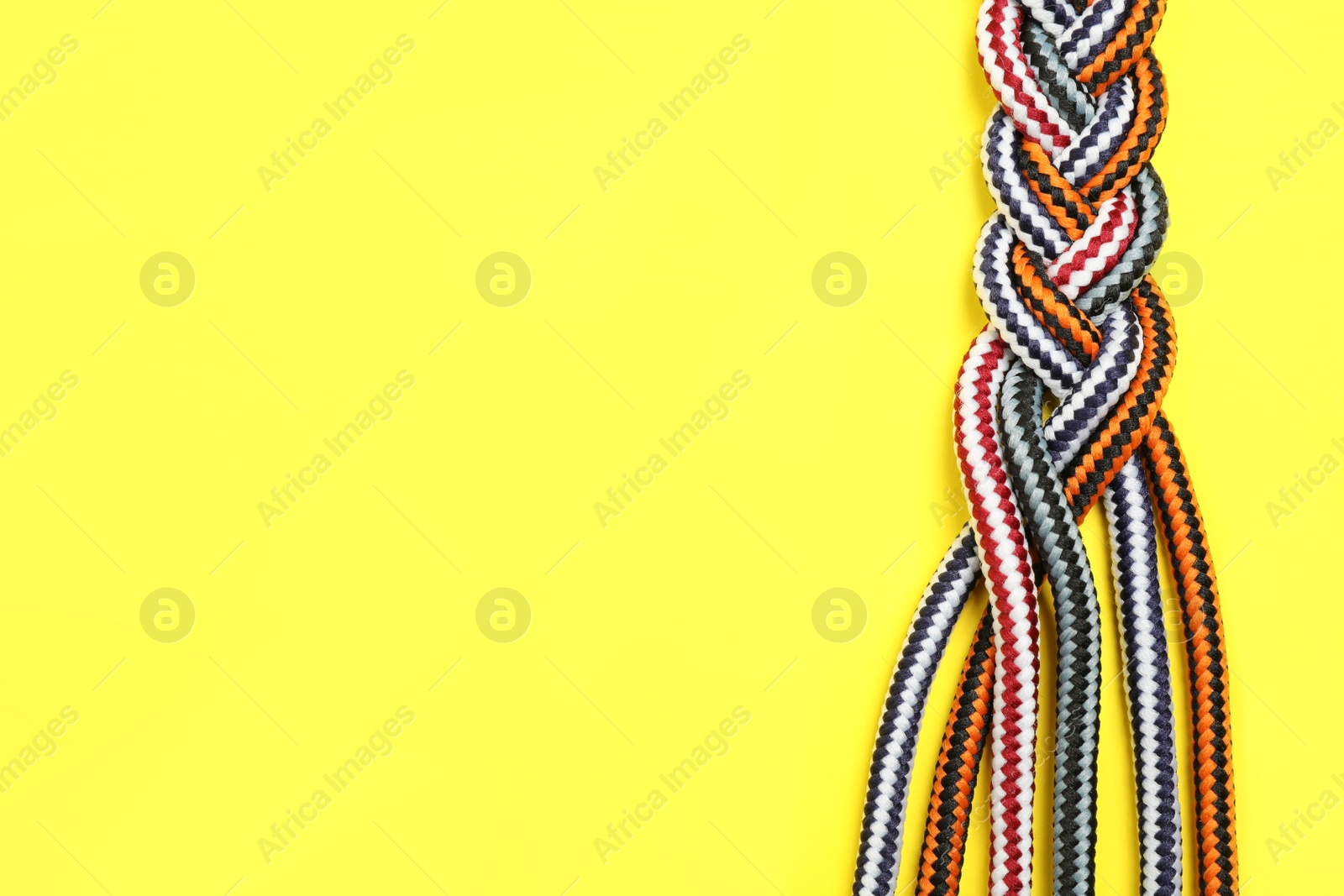 Photo of Top view of braided colorful ropes on yellow background, space for text. Unity concept