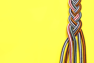 Top view of braided colorful ropes on yellow background, space for text. Unity concept