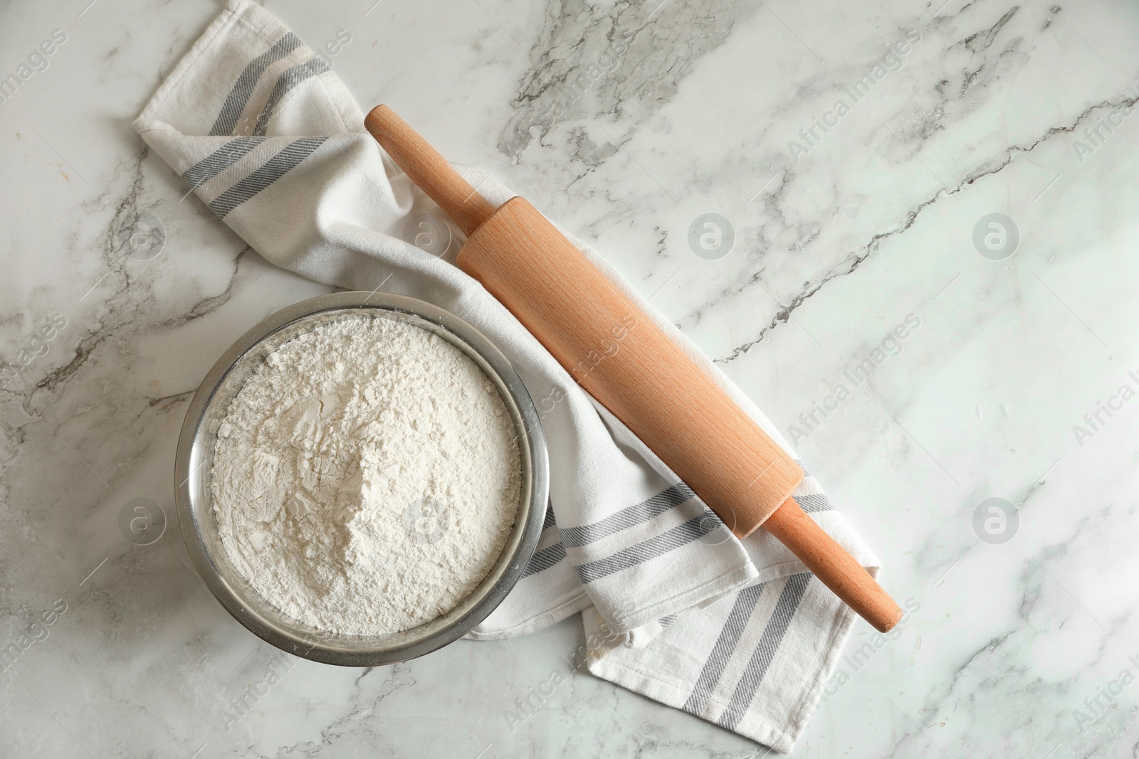 Photo of Flour in bowl, rolling pin and napkin on white marble table, top view. Space for text