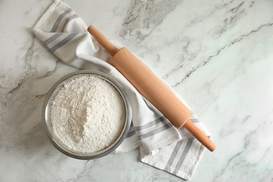 Photo of Flour in bowl, rolling pin and napkin on white marble table, top view. Space for text