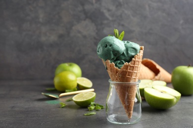 Photo of Composition with delicious spirulina ice cream cone on table against grey background. Space for text
