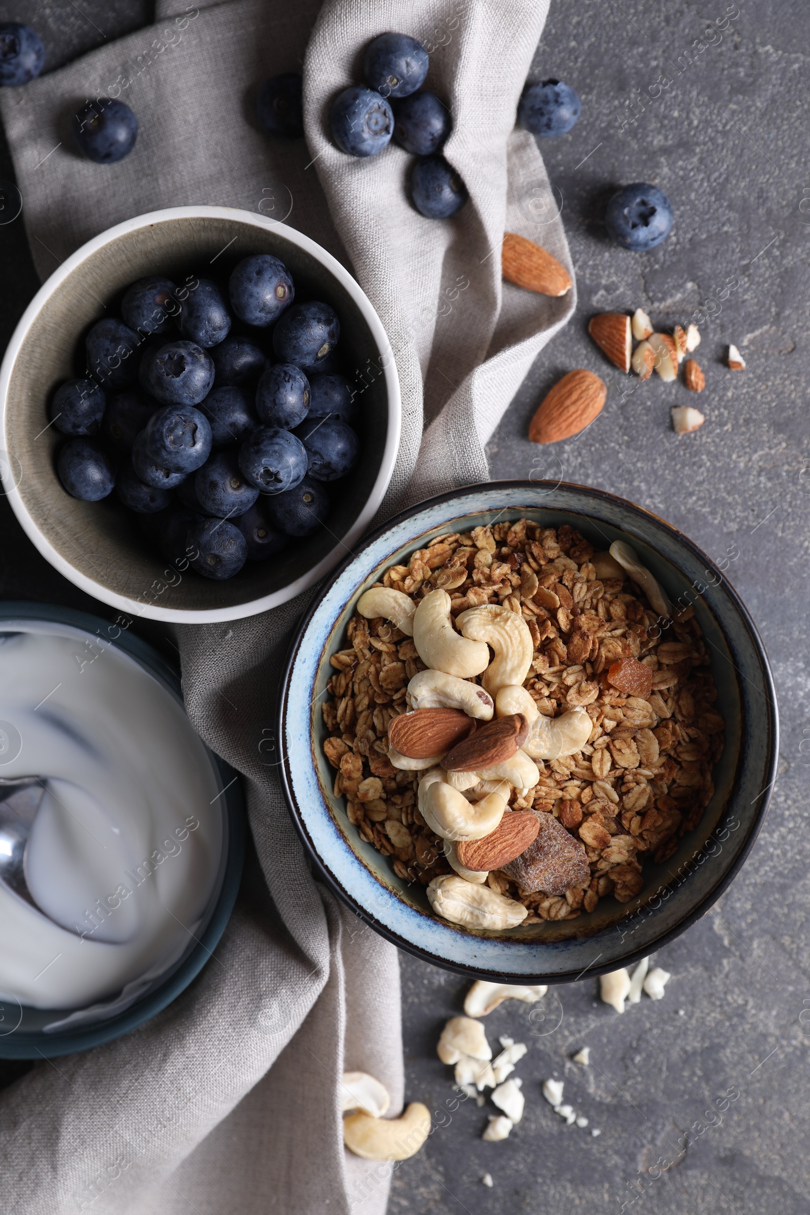 Photo of Tasty granola in bowl, blueberries and yogurt on gray textured table, flat lay