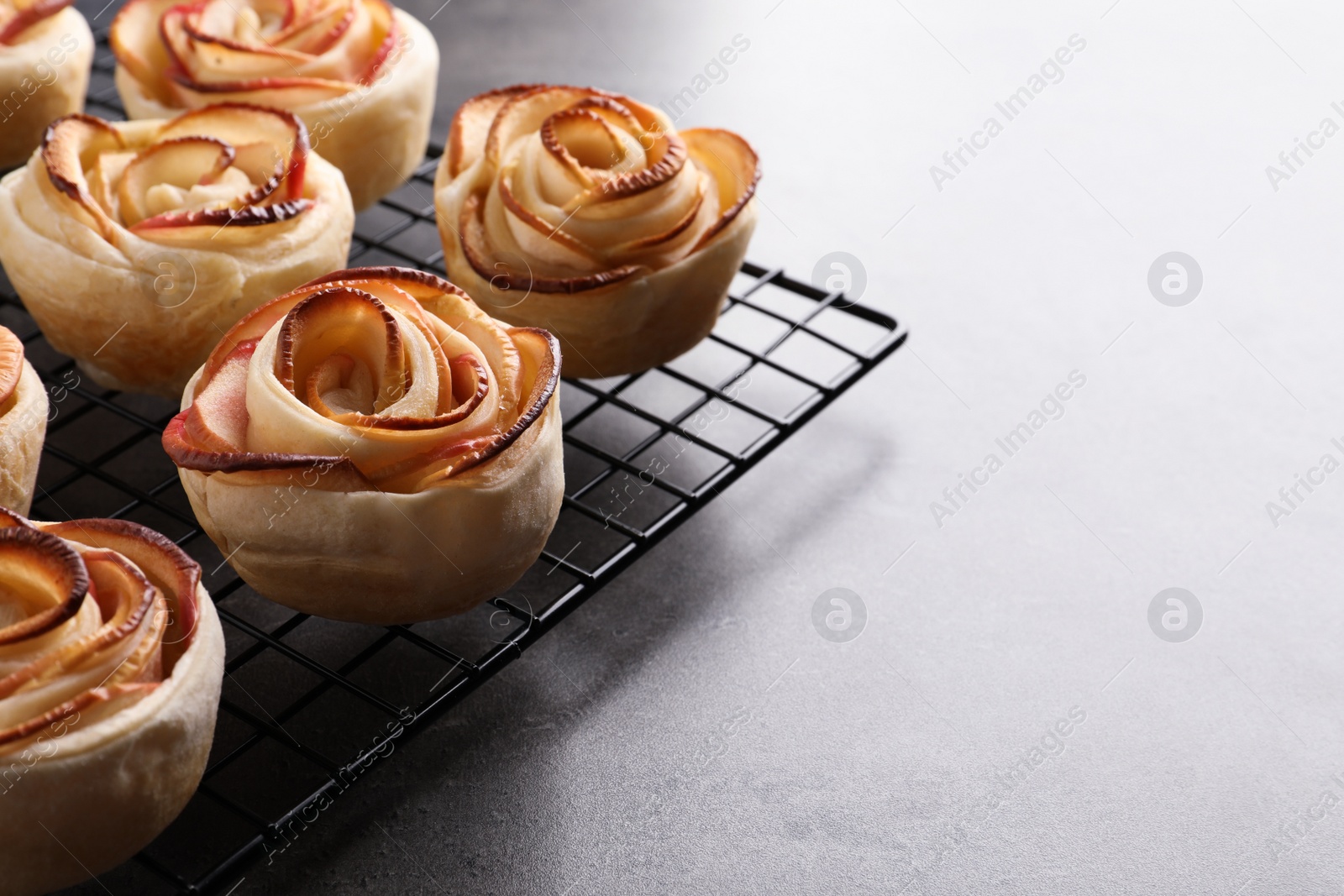 Photo of Cooling rack with freshly baked apple roses on grey table, closeup. Space for text