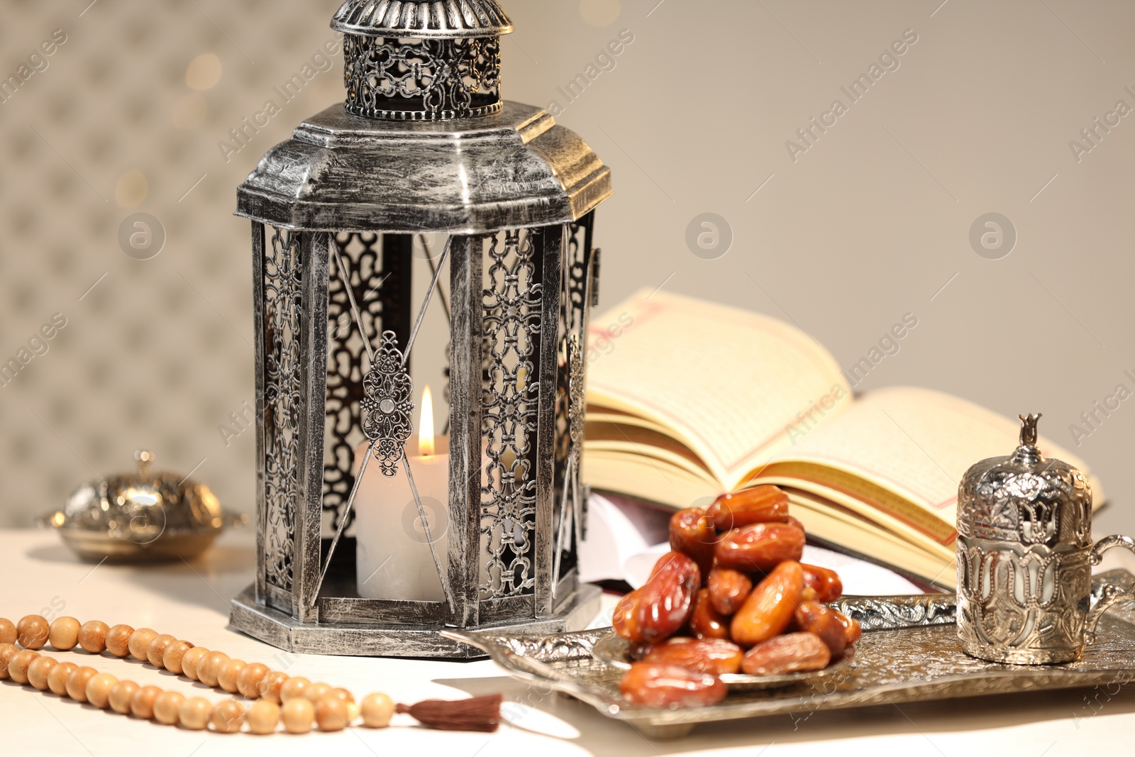 Photo of Arabic lantern, Quran, misbaha and dates on white table