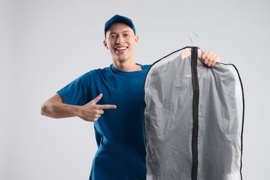 Photo of Dry-cleaning delivery. Happy courier holding garment cover with clothes on light grey background