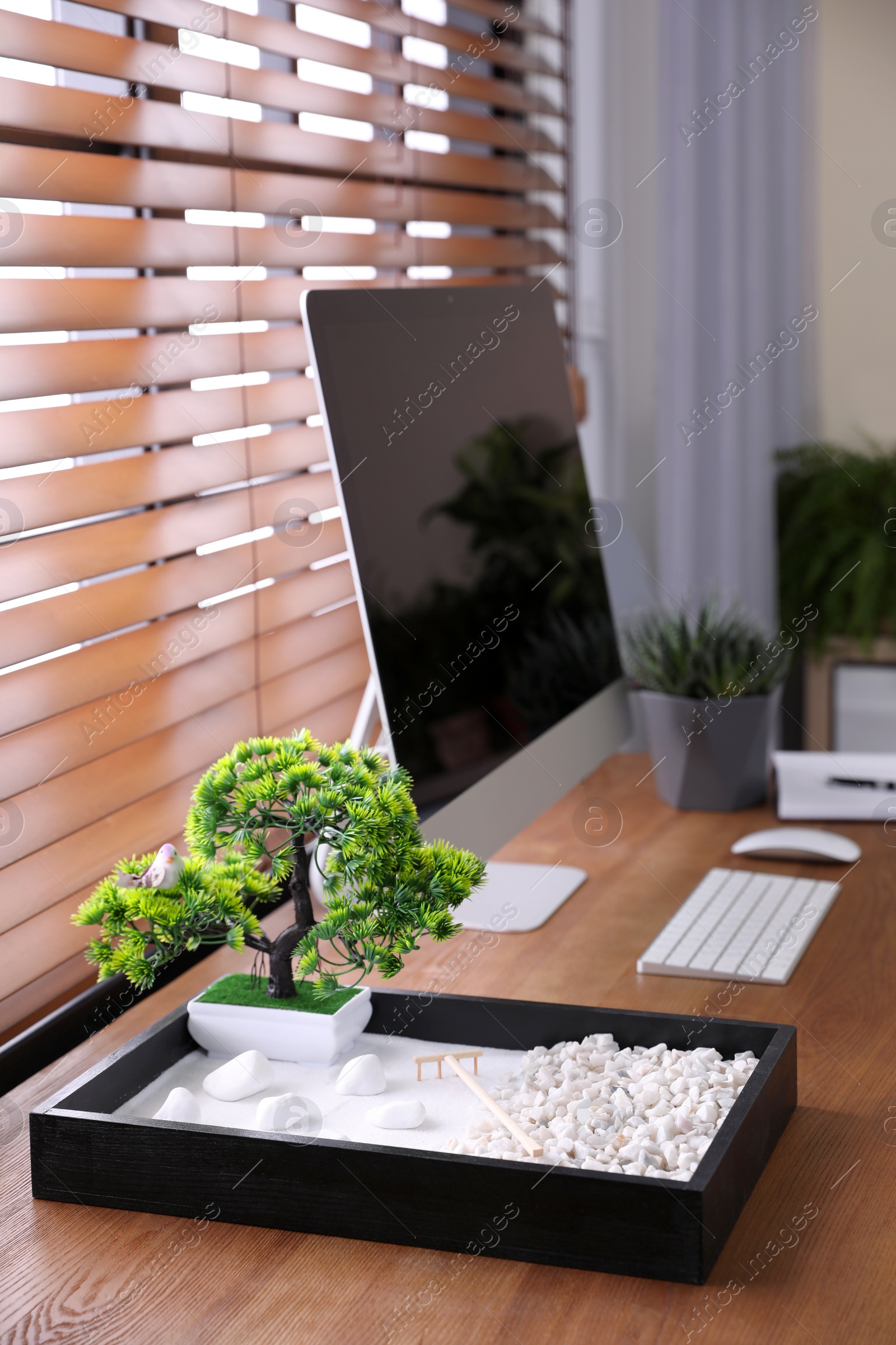 Photo of Modern workplace with beautiful miniature zen garden and computer in room