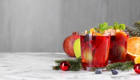 Photo of Aromatic Sangria drink in glasses, ingredients and Christmas decor on white marble table, space for text