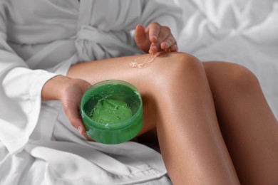 Photo of Young woman applying aloe gel onto her leg on bed, closeup