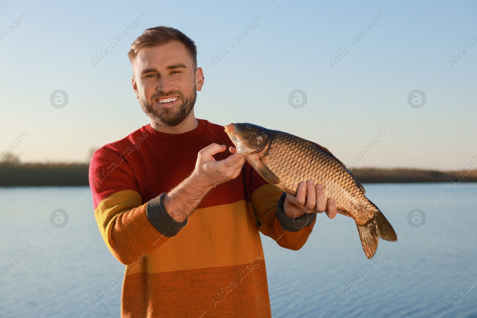 Photo of Fisherman holding caught fish at riverside. Recreational activity