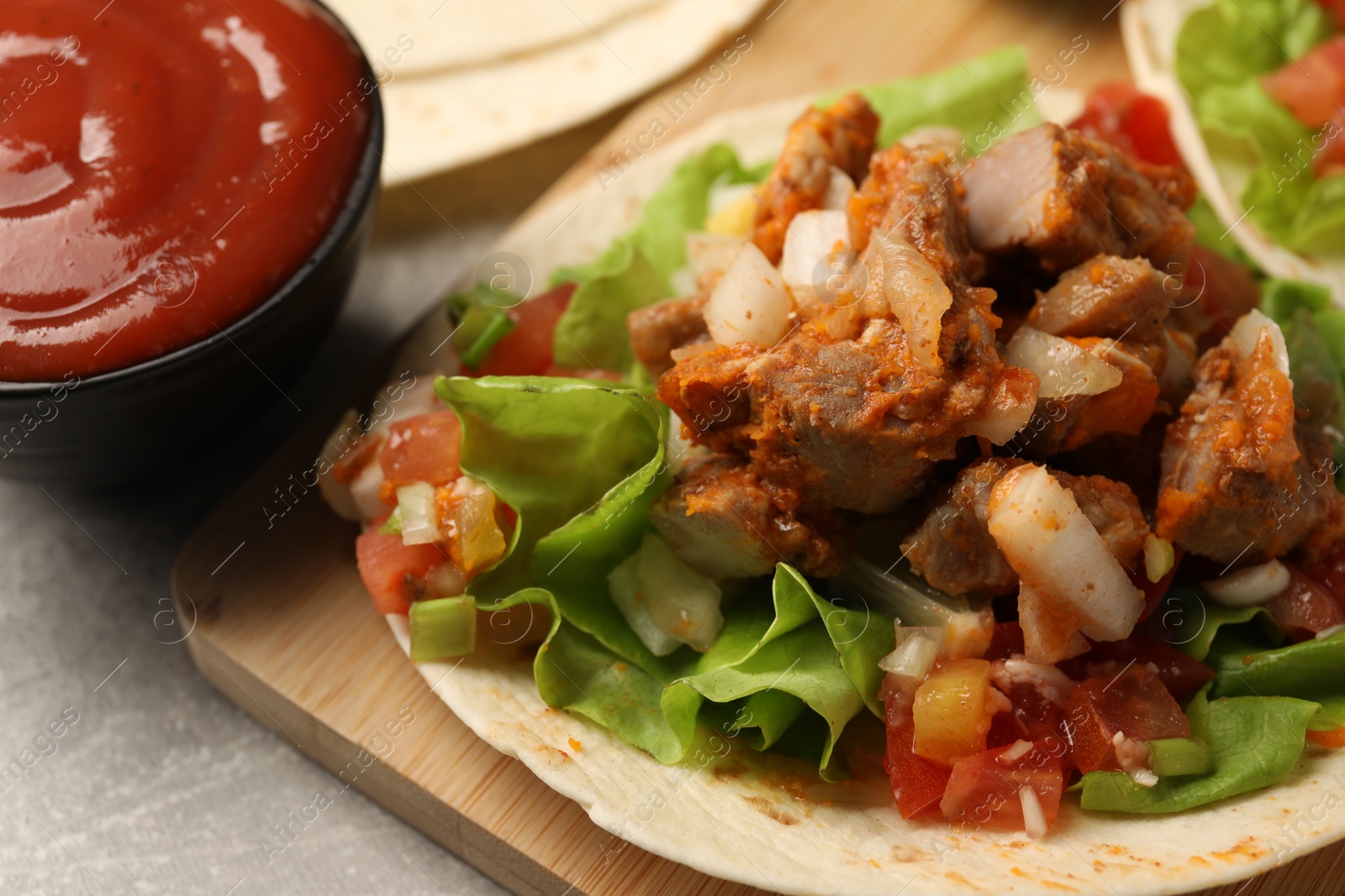 Photo of Delicious tacos with vegetables, meat and ketchup on grey textured table, closeup