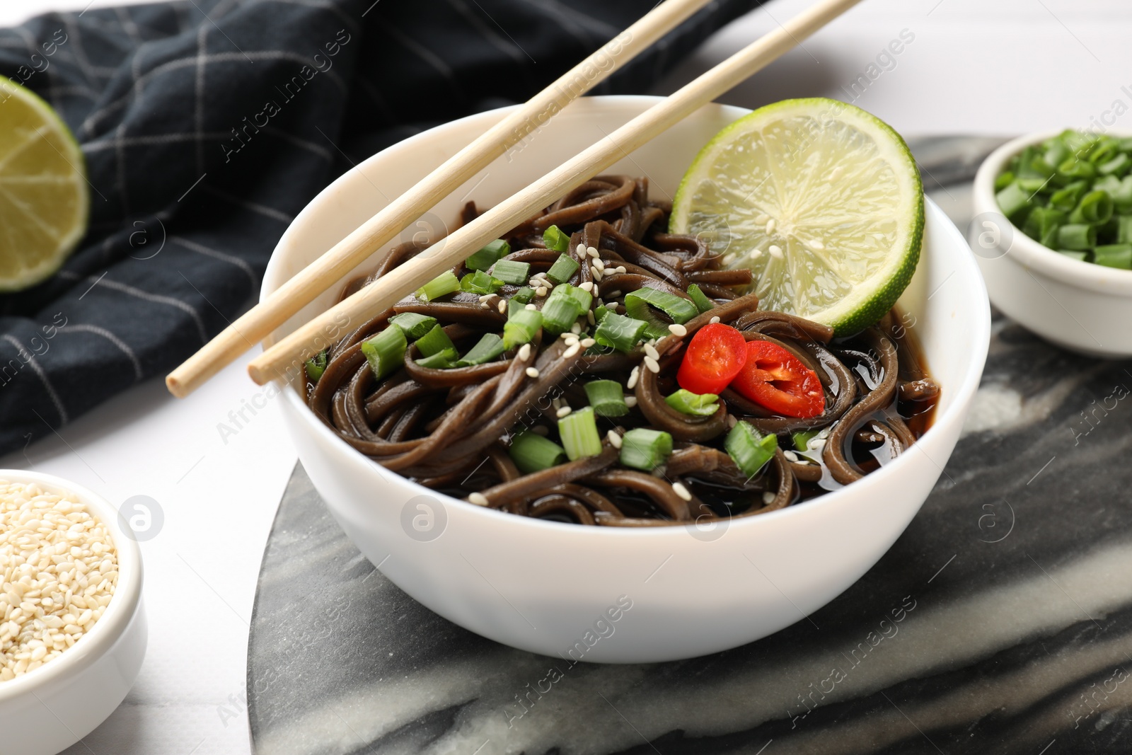 Photo of Tasty buckwheat noodles (soba) with sauce, onion in bowl and chopsticks on white table