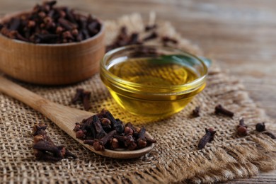 Essential oil and dried cloves on wooden table, closeup
