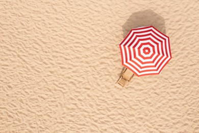 Image of Striped beach umbrella near wooden sunbed on sandy coast, aerial view. Space for text