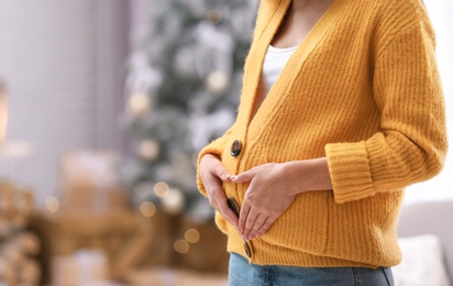 Young pregnant woman in room decorated for Christmas, closeup. Space for text