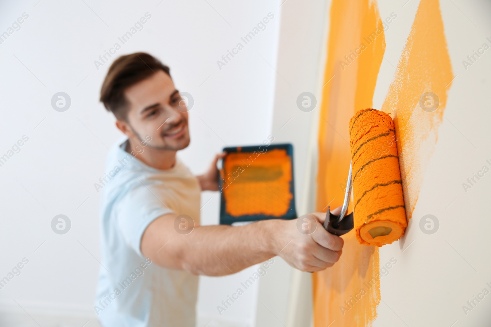 Photo of Happy young man painting wall indoors. Home repair