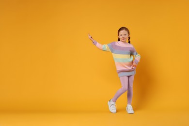 Photo of Cute little girl dancing on orange background, space for text