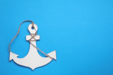 Photo of White anchor with hemp rope on light blue background, top view. Space for text