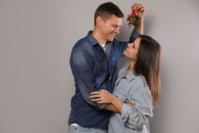 Happy couple standing under mistletoe bunch on grey background