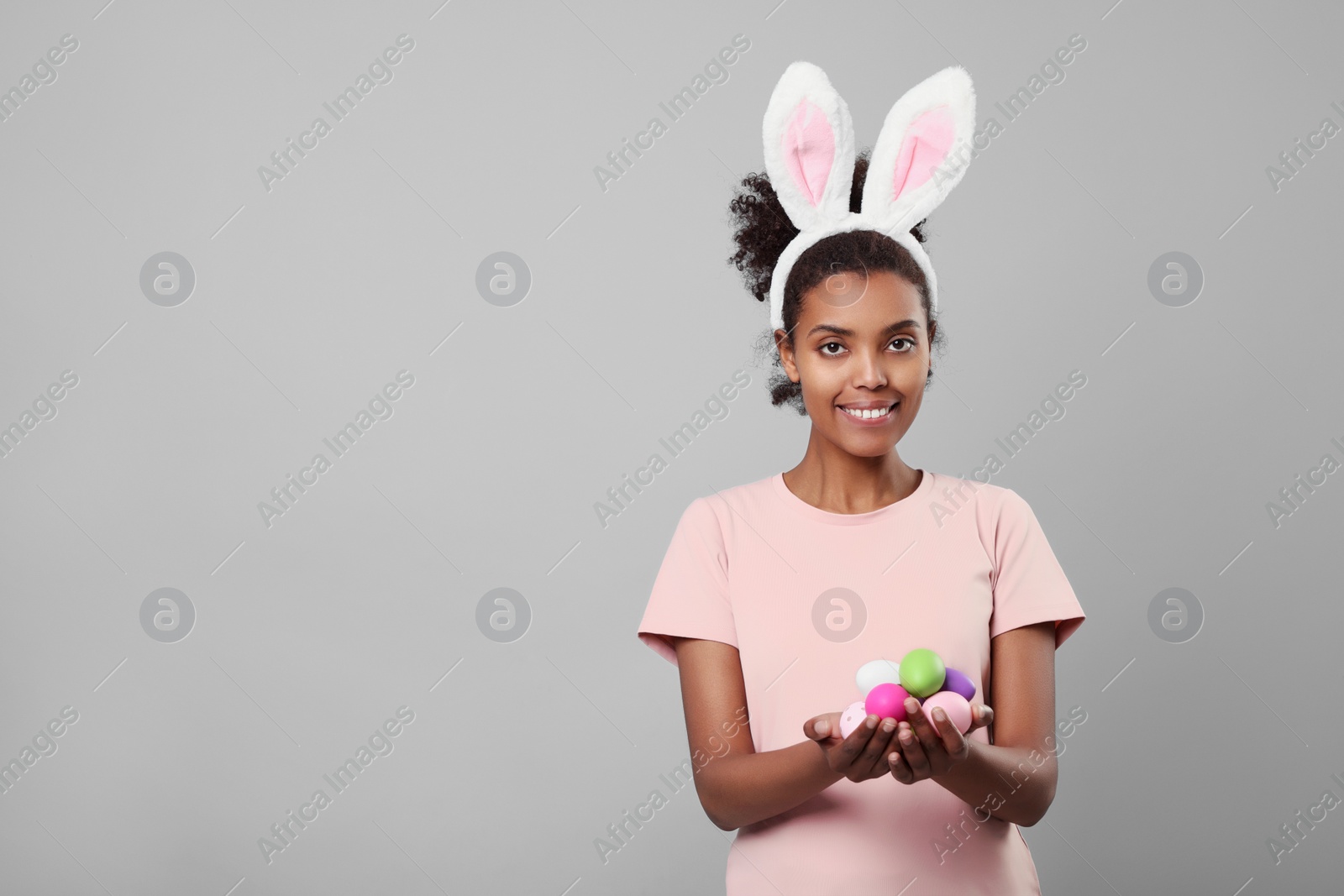 Photo of Happy African American woman in bunny ears headband with Easter egg on gray background, space for text