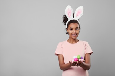 Happy African American woman in bunny ears headband with Easter egg on gray background, space for text
