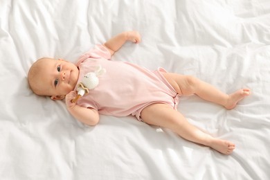 Photo of Cute little baby with toy on white sheets, top view