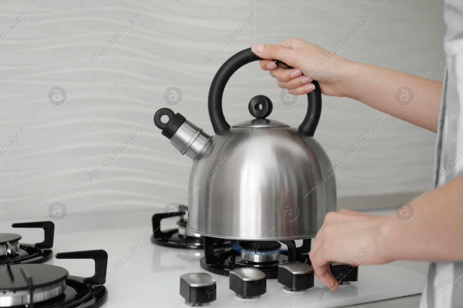 Photo of Woman putting kettle on gas stove in kitchen, closeup