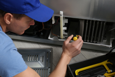 Male technician with screwdriver repairing refrigerator indoors