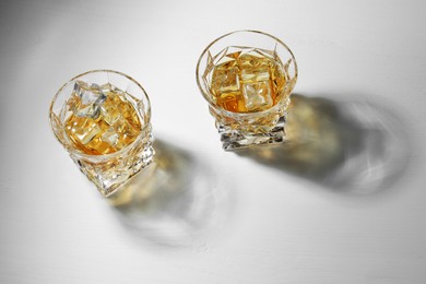 Whiskey with ice cubes in glasses on white table, above view