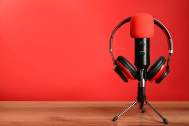 Photo of Microphone and modern headphones on wooden table against red background, space for text