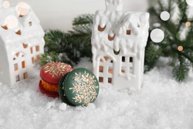 Different decorated Christmas macarons on table with artificial snow, space for text