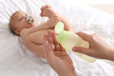 Mother with bottle of massage oil near baby on bed, closeup