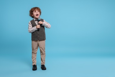 Cute little boy with microphone singing on light blue background, space for text