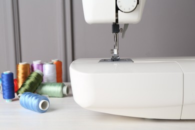 Photo of Sewing machine and spools of threads on white wooden table, closeup