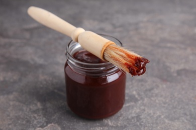 Photo of Jar with barbecue sauce and brush on grey background